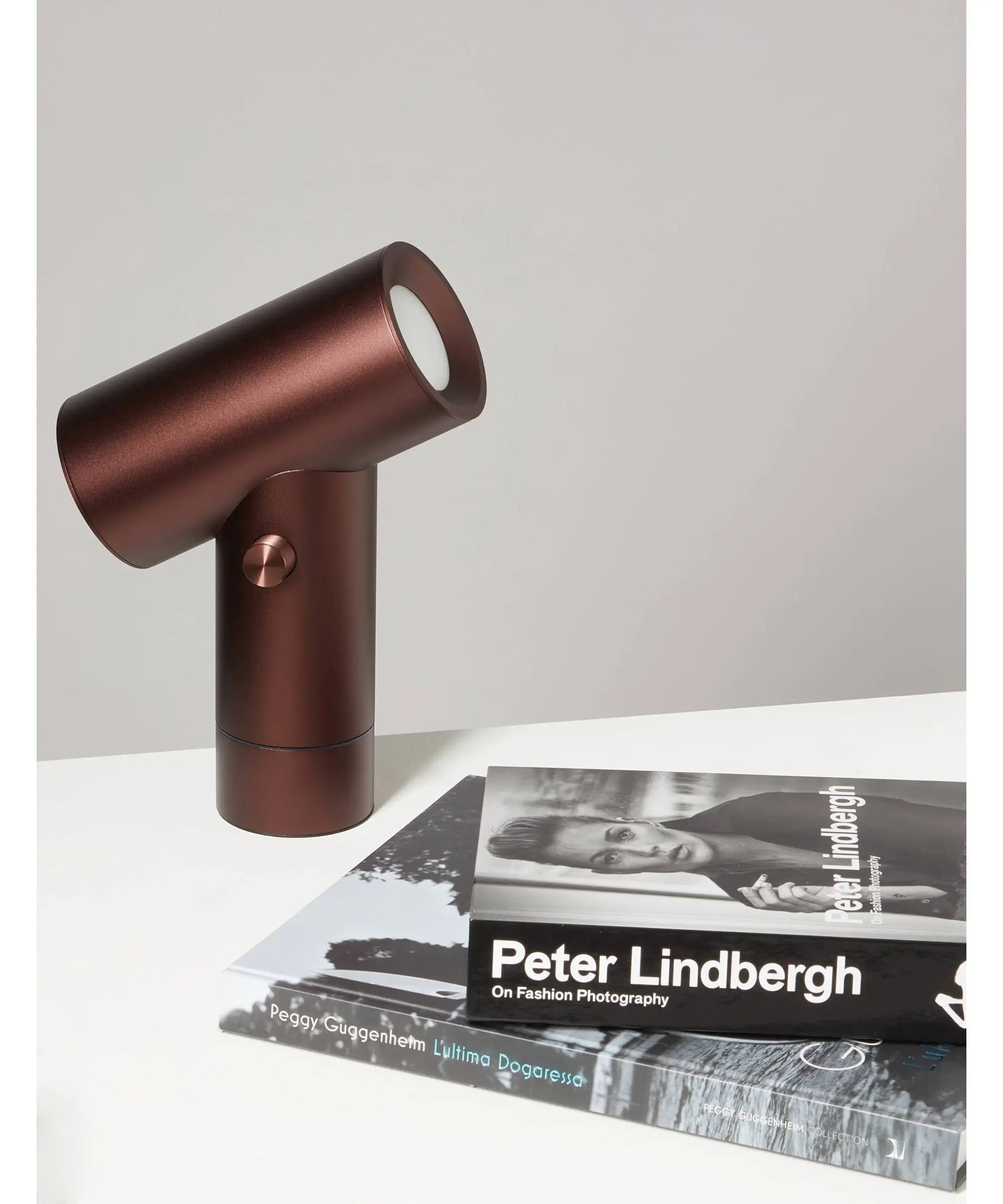 Lampada da tavolo Muuto Beam in alluminio anodizzato bordeaux ambientata su tavolo in interno con libri