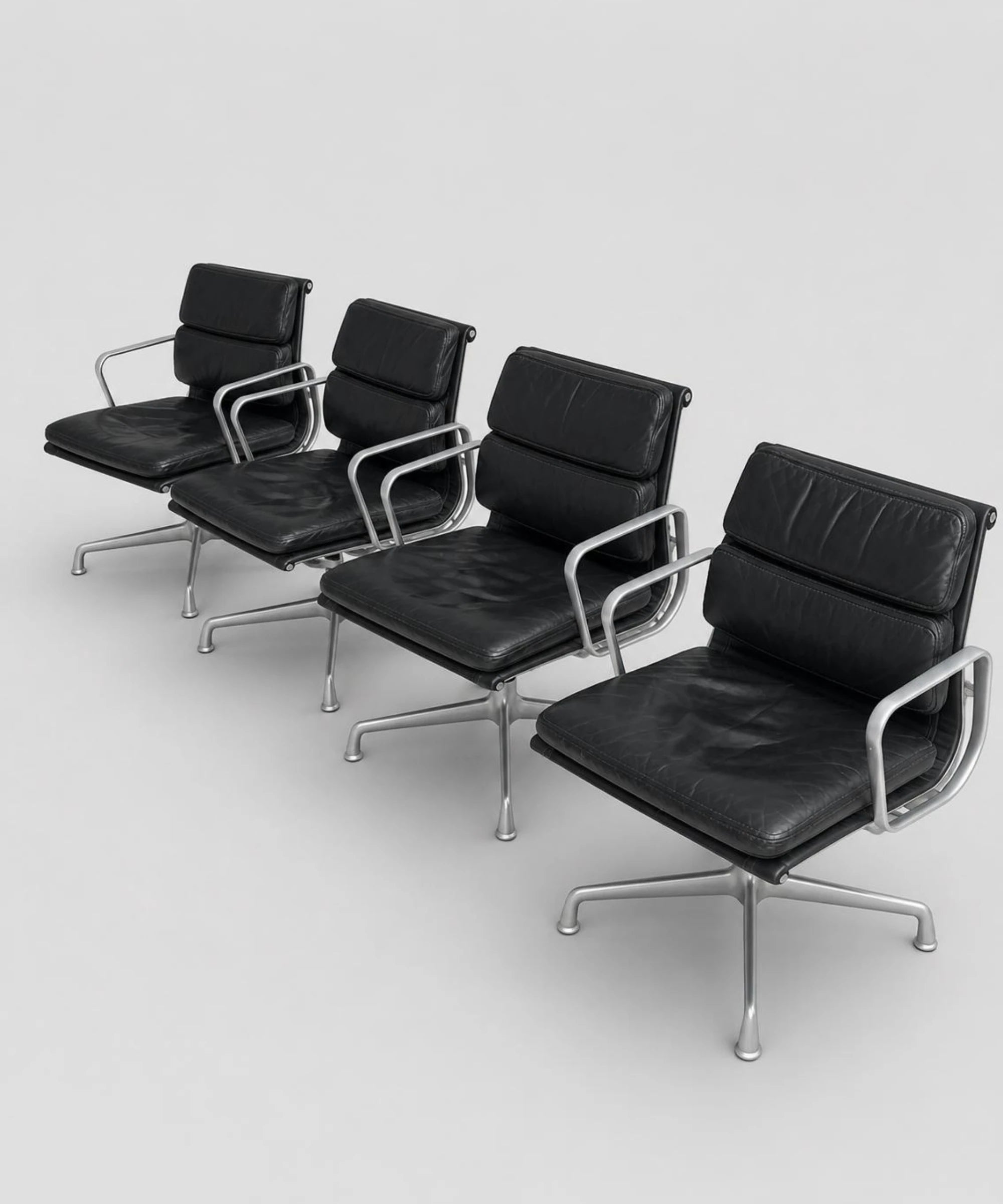Set di quattro sedie ICF EA 208 Soft Pad in pelle nera con base girevole a quattro razze in alluminio viste su sfondo neutro