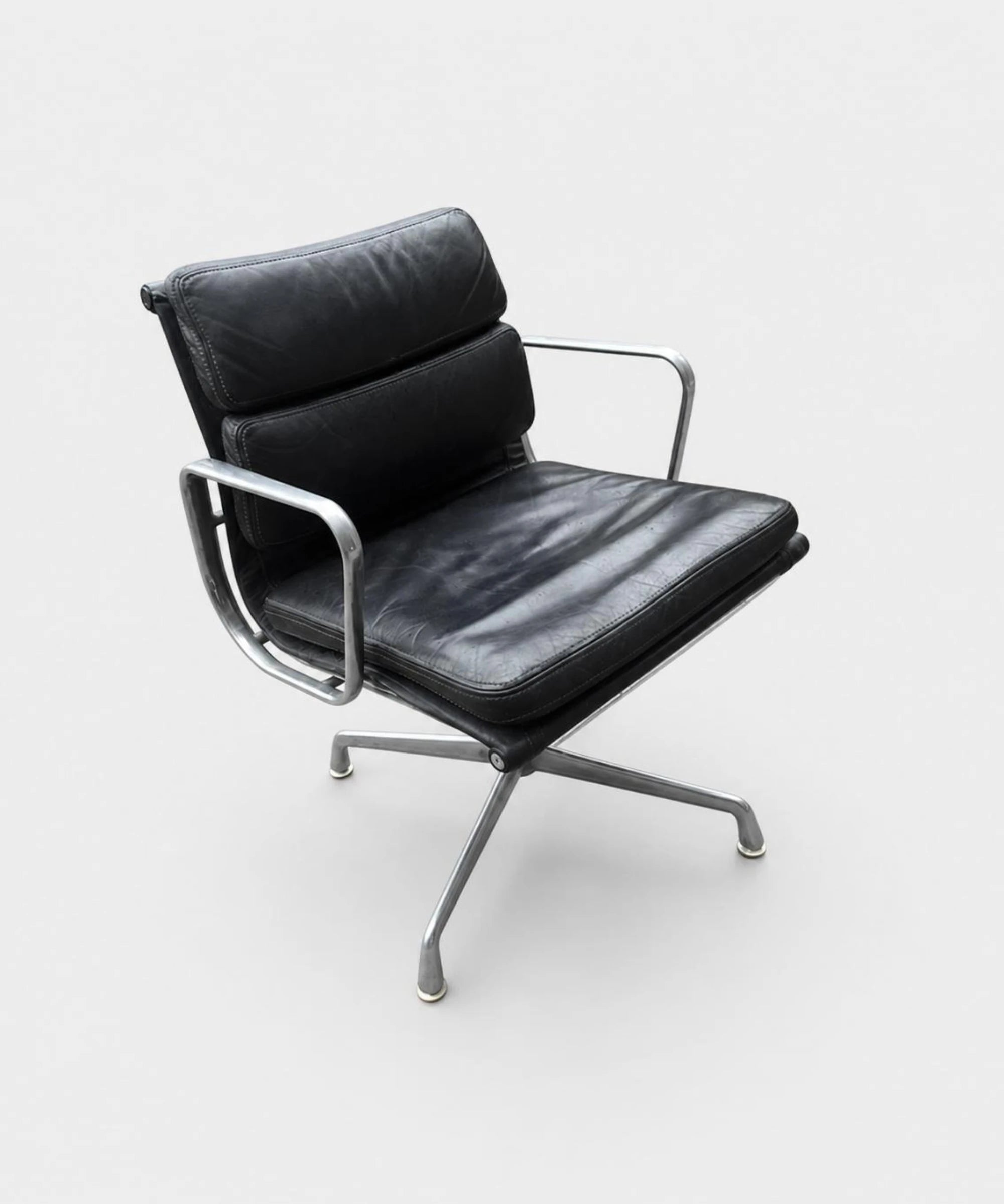 Sedia ICF EA 208 Soft Pad in pelle nera con cuscini imbottiti base girevole a quattro razze in alluminio lucidato con braccioli design Charles & Ray Eames vista su sfondo neutro