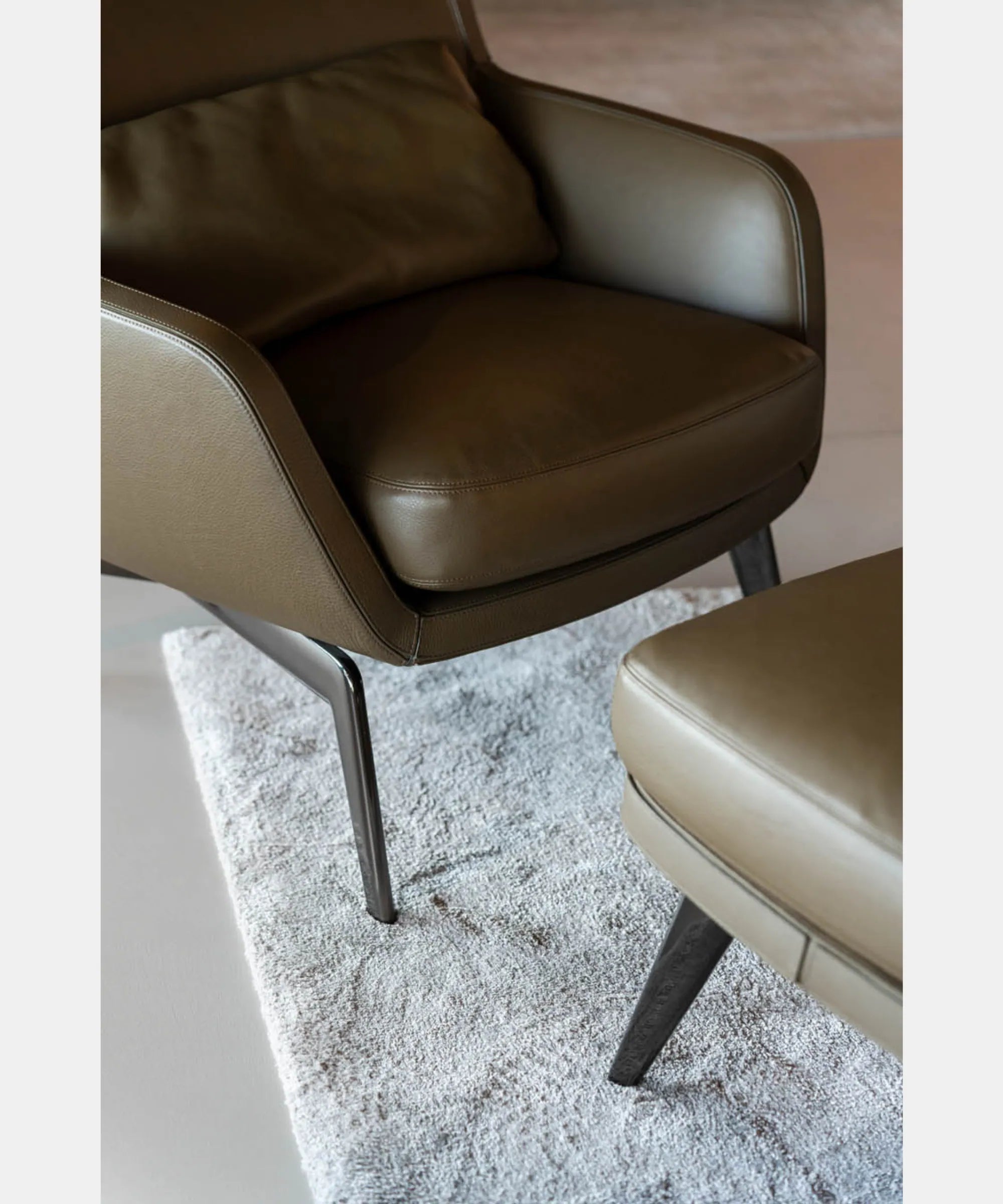 Dettaglio della seduta e del bracciolo della poltrona Minotti Belt con pouf coordinato, rivestiti in pelle, con cuciture a vista e struttura in metallo scuro.
